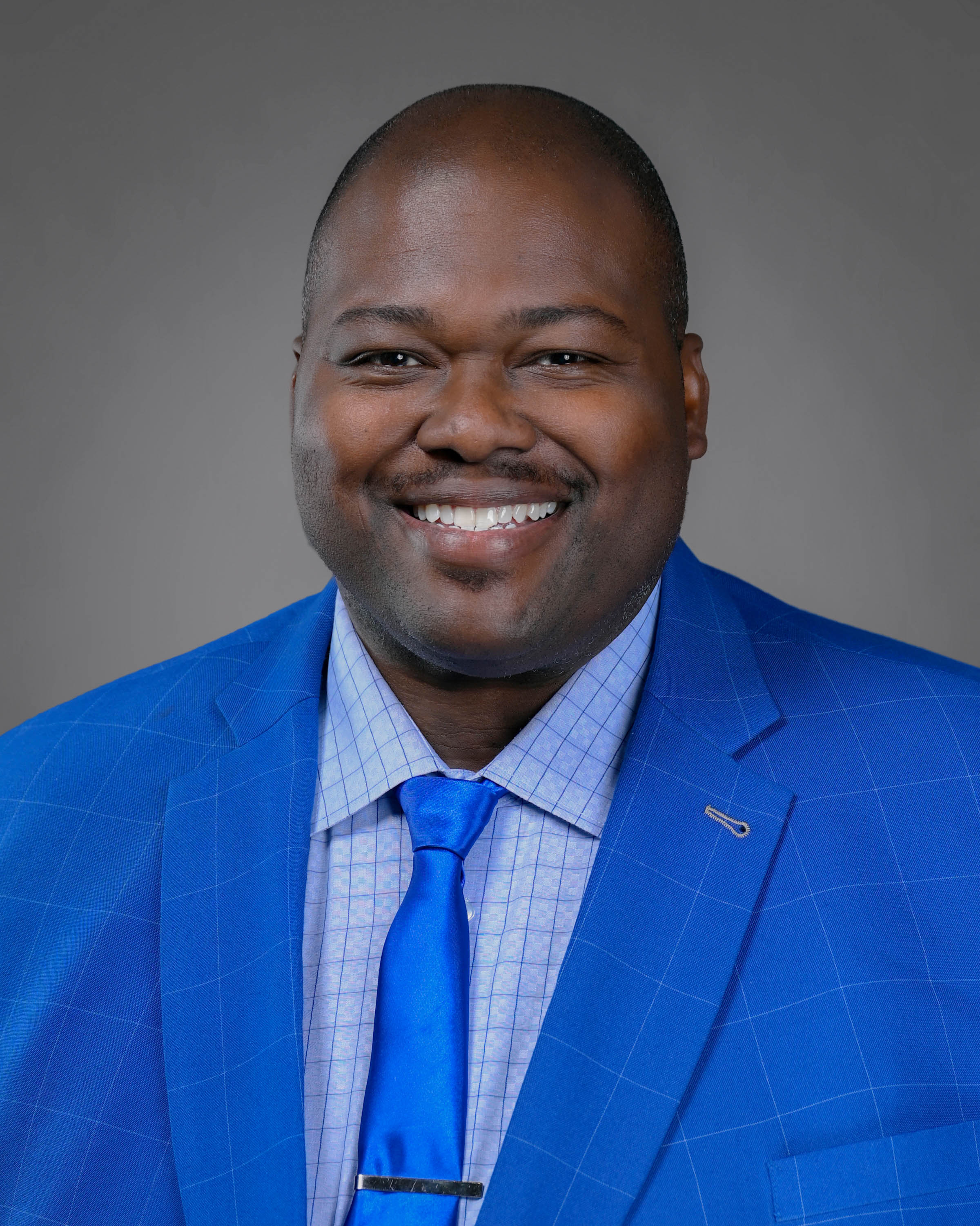 Kind smiling man with short hair and clean shaven in a blue striped shirt with a lighter blue shirt and tie